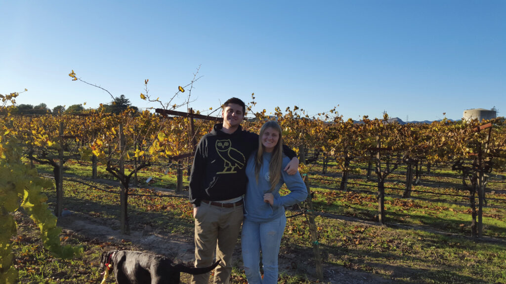 Young man and woman with their arms around each other in the vineyard with fall colored leaves